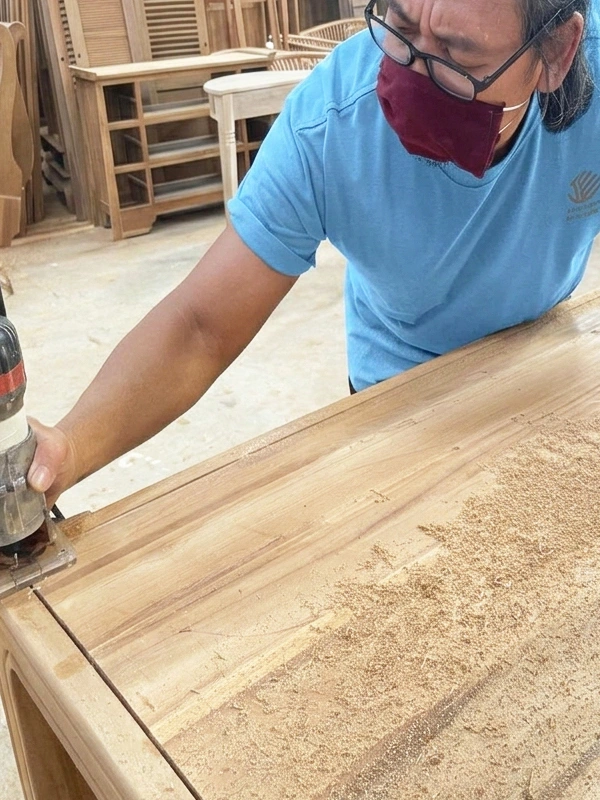 Worker sanding solid teak wood furniture surface